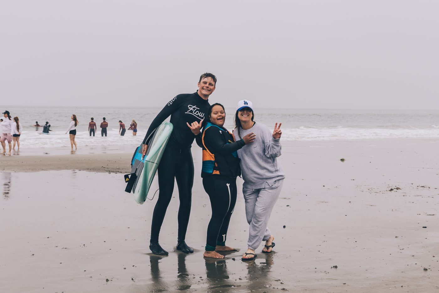 A Flow coach and two young surfers throwing peace signs on the beach