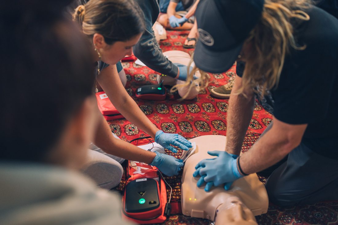 Trainees practice chest compressions and AED use on a CPR manikin with gloves on
