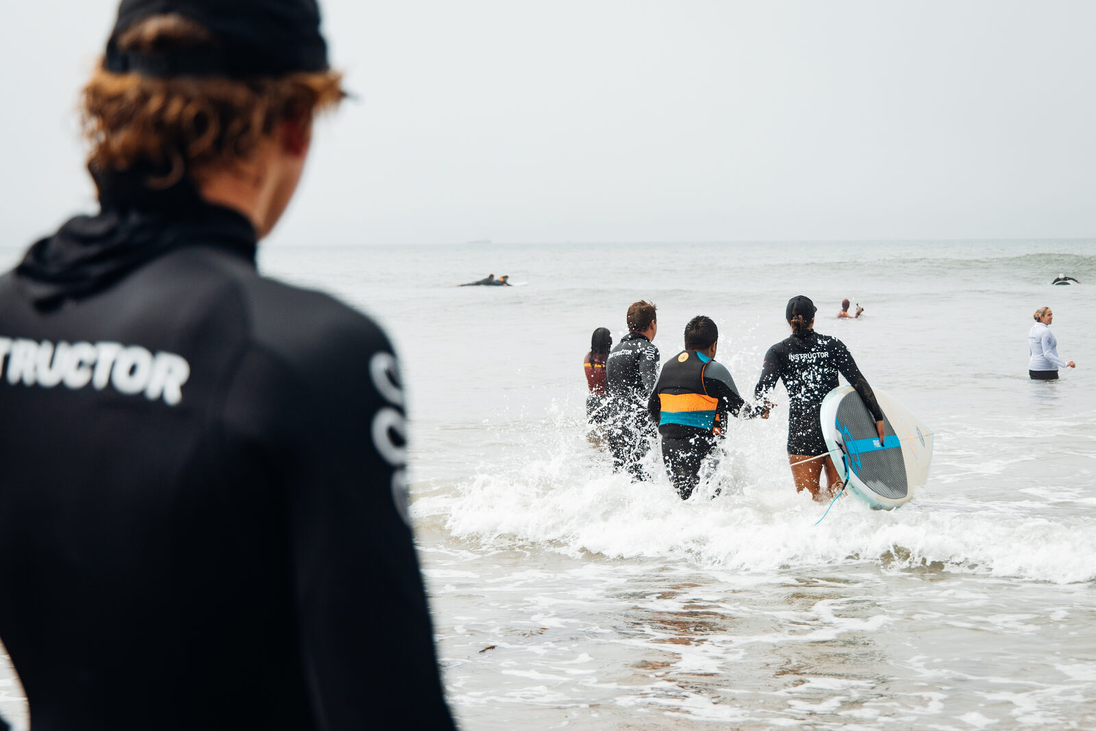 A Flow instructor watches from the shore as coaches walk an athlete out into the surf