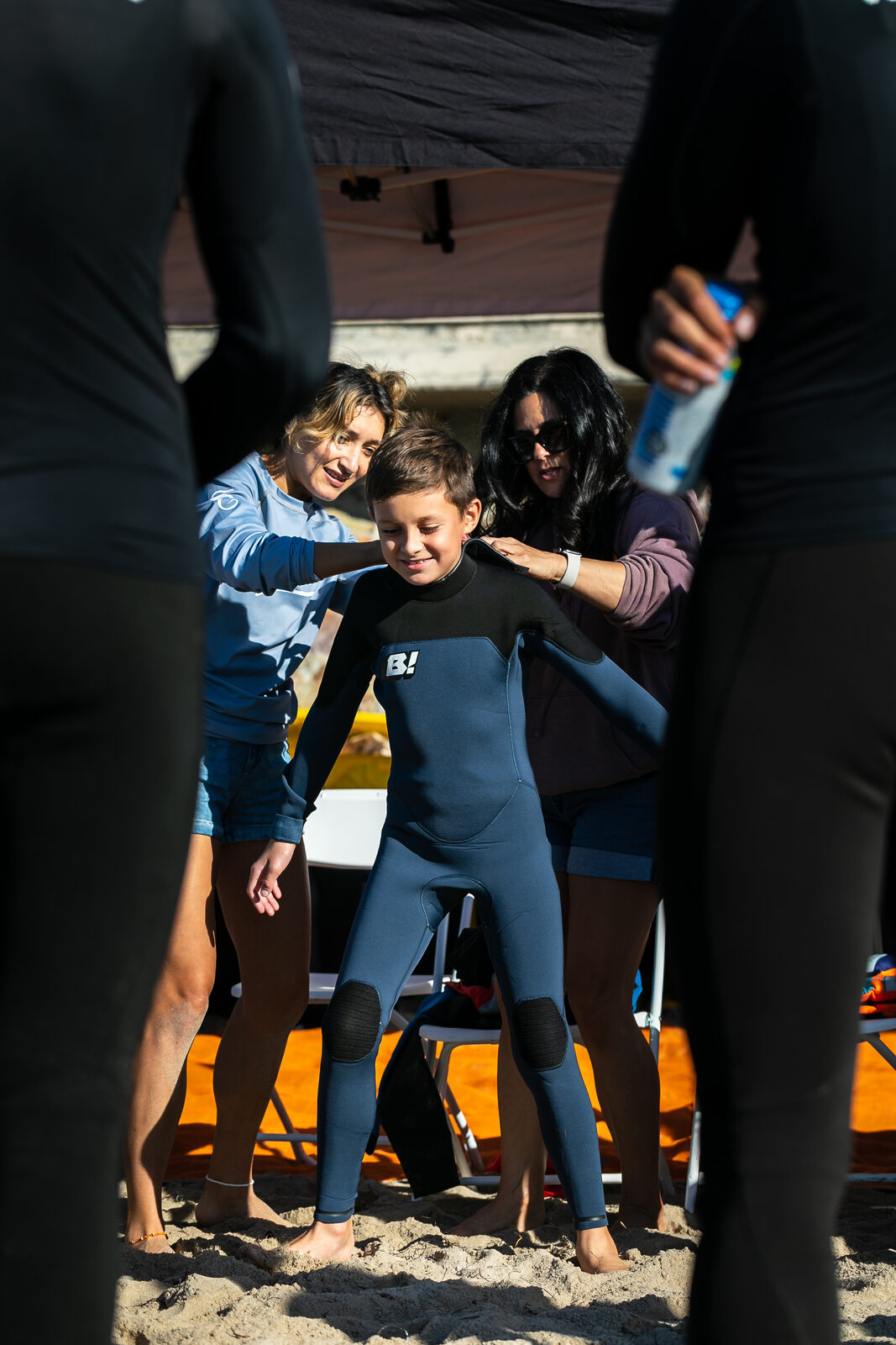Volunteers help a young athlete into a wetsuit under the Flow tent before a session