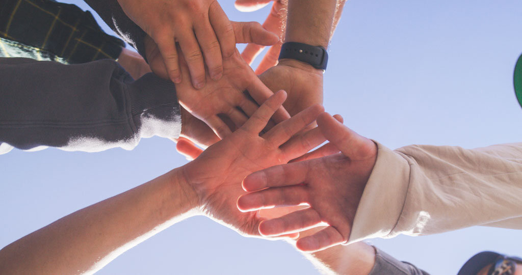 Flow athletes, coaches, and volunteers stack their hands together under a blue sky