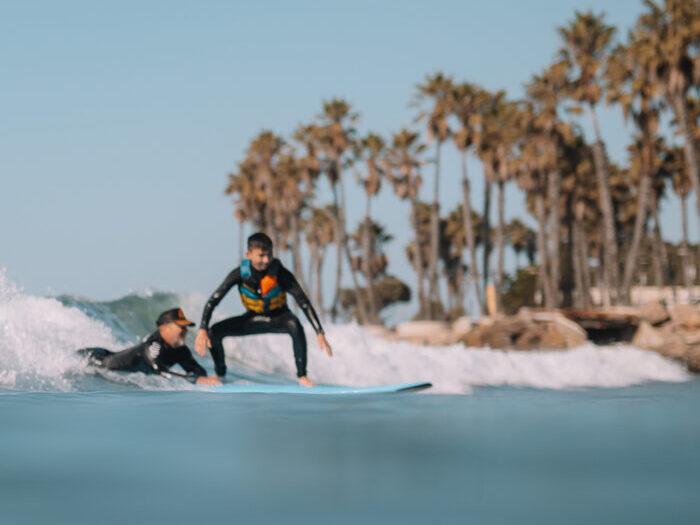 A young athlete rides a wave standing on his own while his Flow coach stays close behind on the board